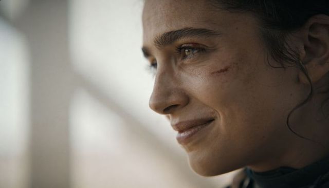 Smiling woman with grazed right cheek looking out through window, cinematic close-up portrait