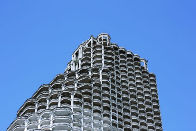 The photo shows an abandoned multi-story building with numerous empty balconies, highlighted against a clear blue sky. This image can be used to represent themes of urban decay, abandoned construction projects, or modern architectural designs. Suitable for urban planning presentations, real estate discussions about unfinished projects, or artistic interpretations of city environments.