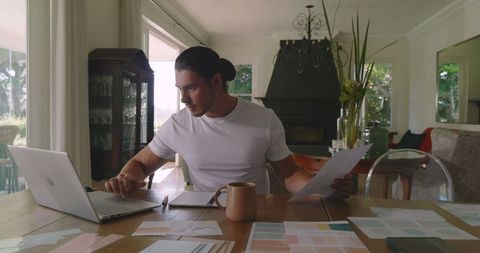 Focused entrepreneur working from home reviewing documents with laptop