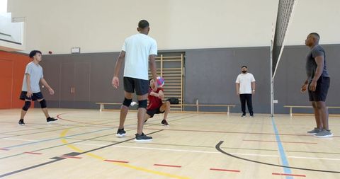 Diverse men playing indoor volleyball on hardwood court showing teamwork and camaraderie