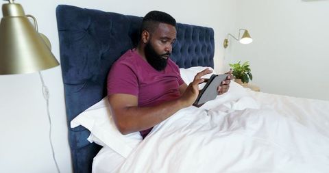 Man Relaxing in Bed Using Tablet in Minimalist Bedroom
