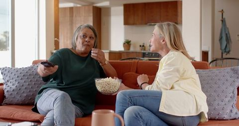 Diverse female friends enjoying popcorn and conversation on modern sofa