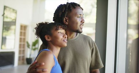 African couple gazing out window in contemporary home embracing with warm connection