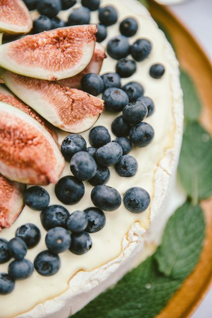 Close-up view of pavlova topped with fresh figs and blueberries, garnished with mint leaves. Suitable for recipes, food blogs, and culinary presentations.