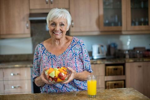 Senior Woman Holding Fruit Salad and Orange Juice in Modern Kitchen