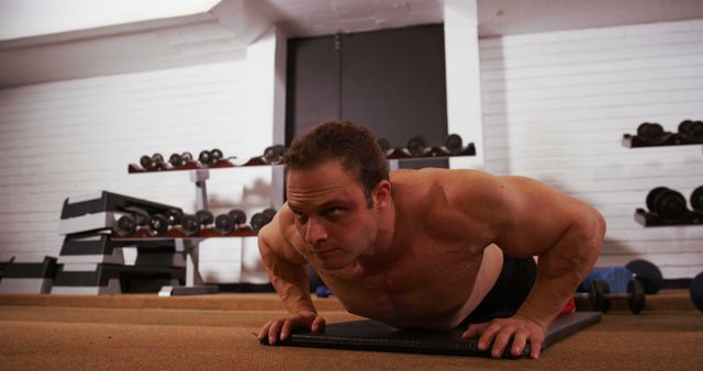 A man performing push-ups in a gym environment, showcasing strength and determination. This visual can be used in fitness and workout programs, gym advertisements, personal training brochures, and health and wellness articles to represent physical fitness, strength training, and exercise routines.