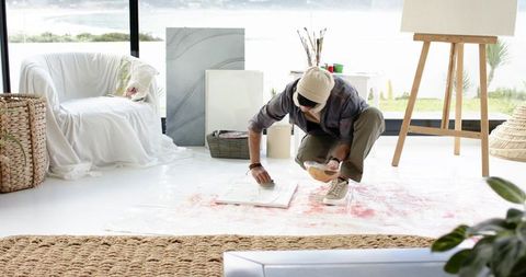 Indian artist kneeling painting abstract canvas on floor in seaside studio natural light