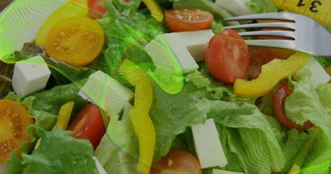 Overhead showing crisp salad with lettuce, tomatoes, feta, fork and measuring tape