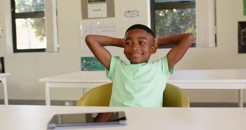 Relaxed African American Boy Leaning Back in Classroom with Tablet on Desk
