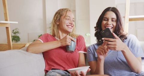 Women relaxing at home using smartphone and eating snacks