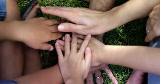 Hands of different family members showing unity and togetherness outdoors on grassy ground. Perfect for use in articles or campaigns about family bonds, trust, teamwork, and support. Can be used for promoting family-centered activities, diversity, or unity.