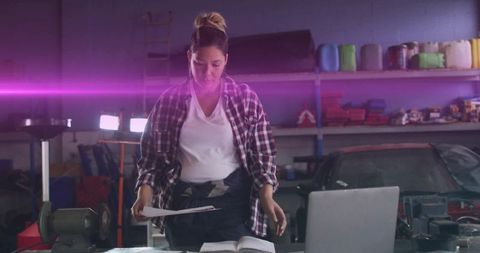 Female Mechanic Studying Manuals and Laptop in Workshop