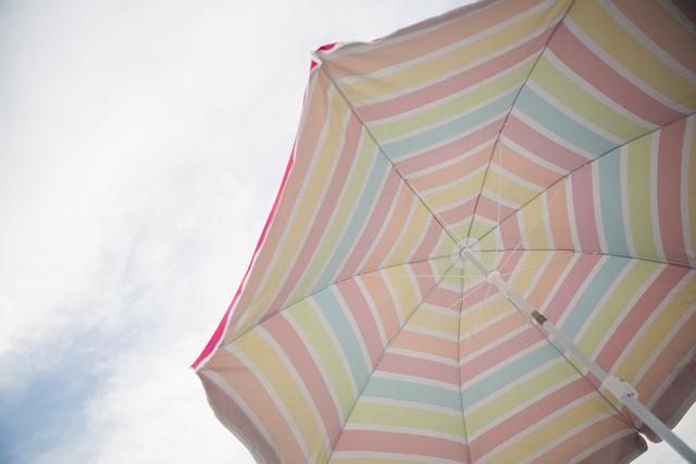 Low angle view of a colorful striped beach umbrella against a blue sky. Ideal for use in summer vacation promotions, travel brochures, outdoor leisure activities, and sun protection products.