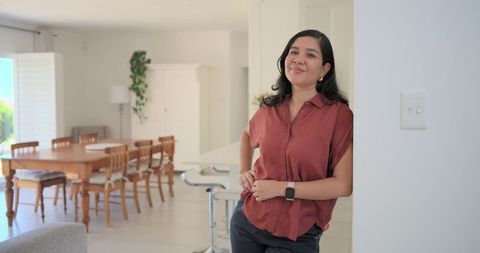 Confident woman leaning in modern open-plan home checking smartwatch in bright daylight