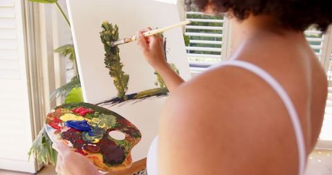 Woman creating landscape painting in sunlit studio