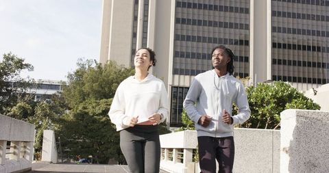 Diverse urban friends jogging together on city walkway wearing hoodies and leggings