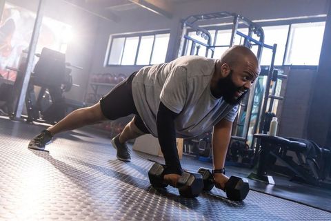 African man holding hex dumbbells in high plank core strength training in modern gym