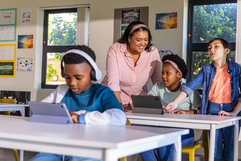 Teacher guiding diverse students with tablets and headphones in bright classroom