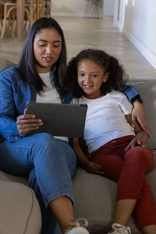 Caregiver and child sharing tablet while relaxing on sofa, bonding during screen time