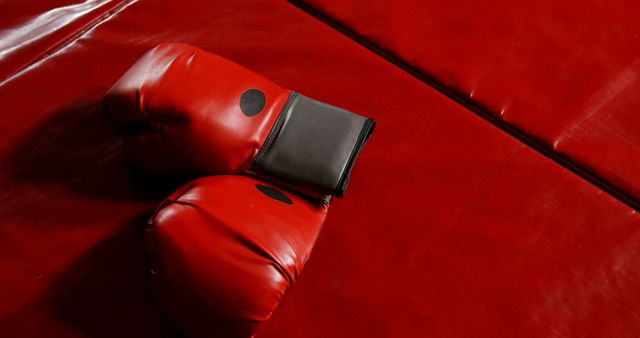 Red boxing gloves resting on a red boxing mat. Gloves symbolize sportsmanship, fitness, and combat training. Ideal for use in content related to boxing, kickboxing, martial arts, fitness training, sports promotions, and athletic equipment advertisements.