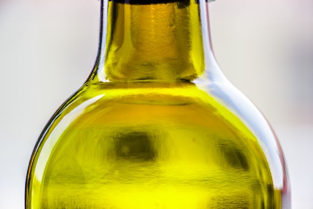 This image features a close-up view of a bottle filled with olive oil. The clear glass and the yellowish hue of the oil are prominently displayed. This shot is great for use in culinary contexts, food blogs, health articles about the benefits of olive oil, or for promoting cooking products.