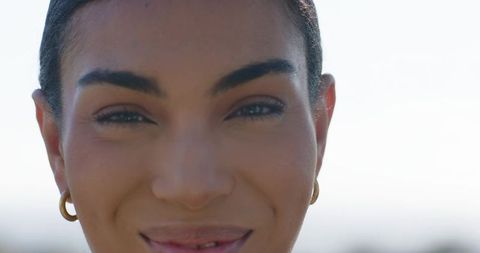 Closeup portrait african woman smiling in sunlight with gold hoop earrings and glowing skin