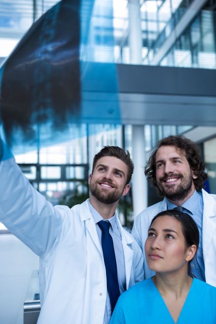 Medical team consisting of doctors and a nurse analyzing an X-ray in a modern hospital environment. This image can be used for healthcare-related content, medical articles, hospital brochures, and educational materials about medical diagnostics and teamwork in healthcare settings.