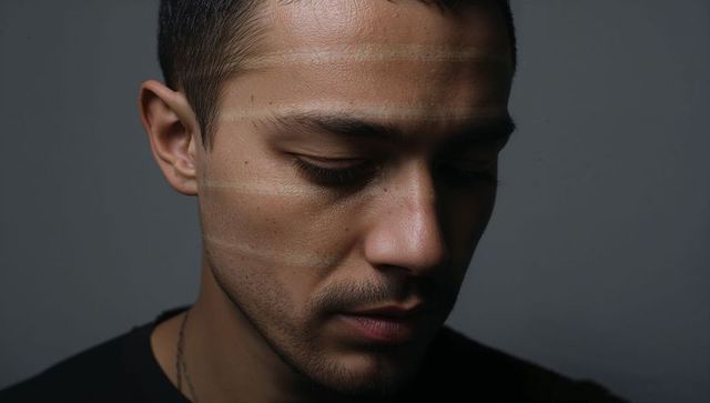 Contemplative man tilting head with banded studio lighting closeup portrait moody texture