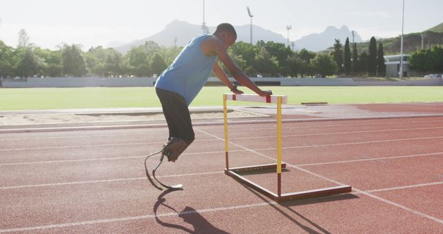 Athlete with prosthetic legs is training on running track while overcoming hurdles. Ideal for content on fitness motivation, adaptive sports, determination, and athletic training.