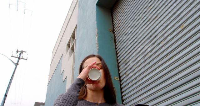 Woman Drinking Coffee Outdoors Near Shuttered Building - Download Free Stock Images Pikwizard.com