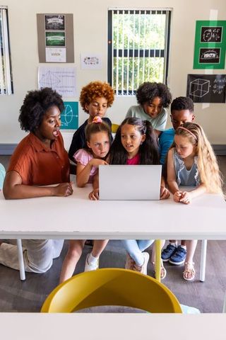African American teacher guiding young students around laptop for hands-on STEM lesson