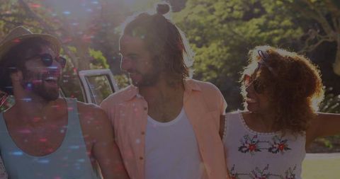 Friends linking arms laughing while strolling on sunlit park pathway, casual summer vibe