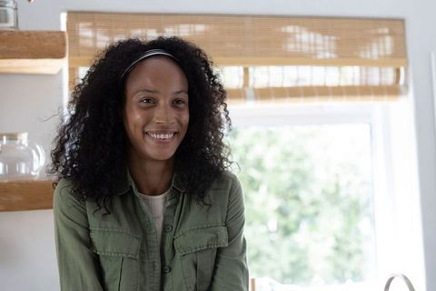Smiling african american woman standing in sunlit kitchen, cozy natural lifestyle