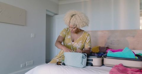 African American woman packing suitcase on bed preparing for weekend getaway with toiletry bag