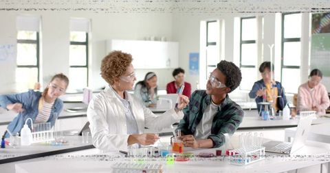 High school science teacher guiding student during chemistry experiment in modern lab