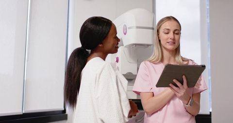 Female radiology technologist explaining mammogram to patient in breast imaging clinic