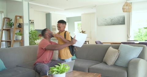 African american father hugging schoolboy with backpack and papers on living room couch