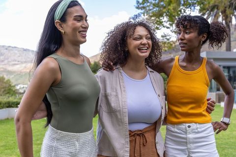 Laughing diverse friends embracing outdoors in casual summer clothing and accessories