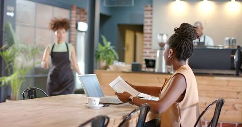 Working woman reviewing documents while using laptop in cozy industrial coffee shop