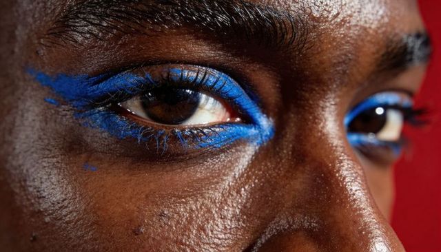 Close-up portrait model wearing electric-blue graphic eyeliner on textured deep skin