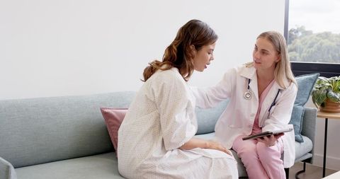 Female doctor comforting patient during clinic consultation on sofa holding tablet