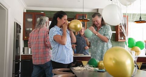 Seniors joyfully inflating balloons in kitchen for celebration