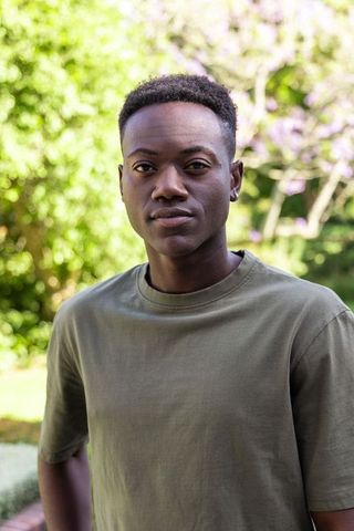 African man standing in garden wearing olive crewneck t-shirt and hoop earring