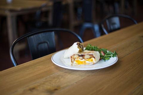 Breakfast burrito sliced revealing eggs and cheese with fresh greens on wooden table
