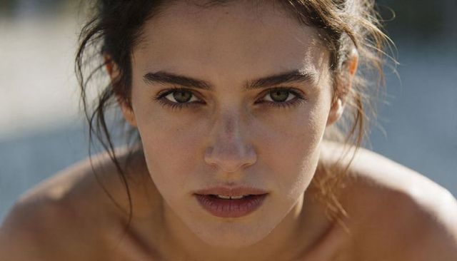 Sunlit closeup portrait of young woman with freckles, natural makeup and pulled-back hair