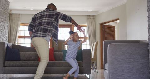 Father and Daughter Joyfully Dancing in Living Room on Colorful Cushions