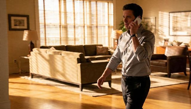 Man walking and talking on smartphone in sunlit modern living room with blinds and couch
