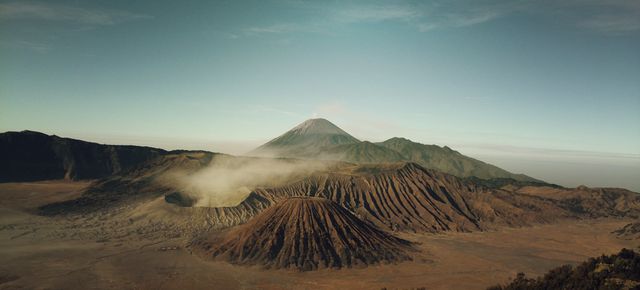 Panoramic view of mountainous landscape featuring prominent volcanoes and mist during sunrise. Serene natural setting ideal for use in travel brochures, adventure magazines, environmental website banners, or as a dramatic nature backdrop in presentations.
