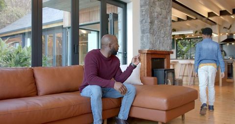 African american father gesturing while son walking toward kitchen in modern rustic living room