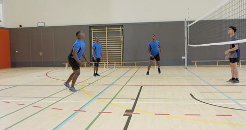 Multicultural male volleyball team training on indoor school gym court wearing blue jerseys